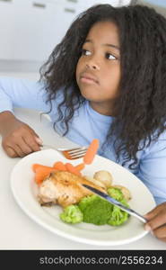 Young girl in kitchen eating chicken and vegetables