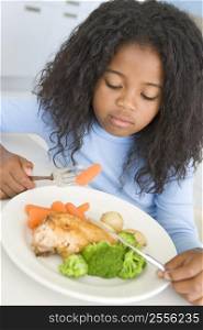 Young girl in kitchen eating chicken and vegetables