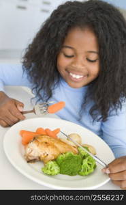 Young girl in kitchen eating chicken and vegetables smiling