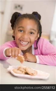 Young girl in kitchen eating cookies smiling