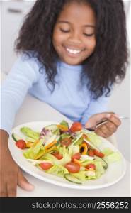 Young girl in kitchen eating salad smiling