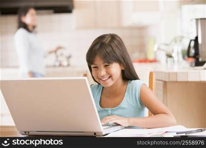 Young girl in kitchen with laptop and paperwork smiling with woman in background