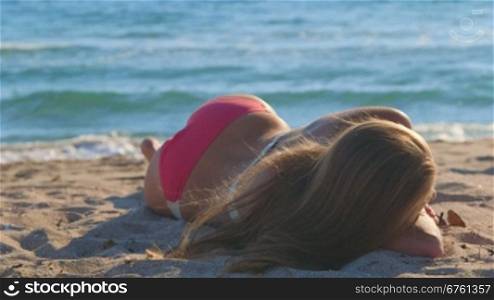 Young girl in pink bikini lying on a sandy beach