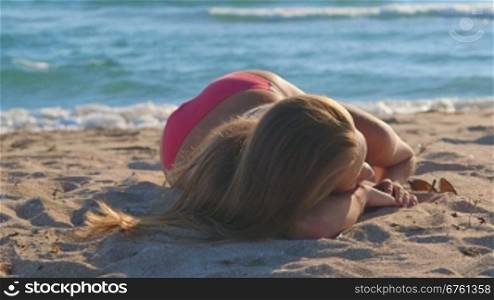 Young girl in pink bikini lying on the sandy beach by sea