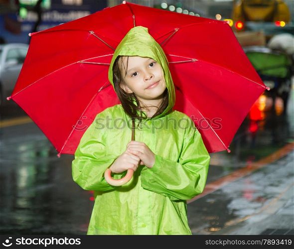 Young girl in rain wearing a green raincoat and holding a red umbrella