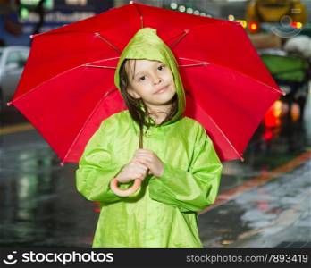 Young girl in rain wearing a green raincoat and holding a red umbrella