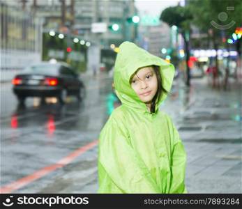 Young girl in rain wearing a green raincoat next to a city street