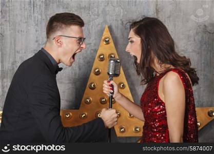 Young girl in red cocktail dress and guy singing with vintage microphone&#xA;