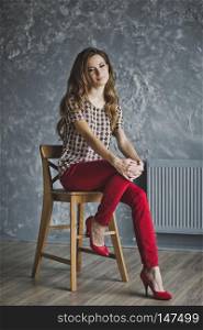 Young girl in red jeans was sitting on a chair.. Studio portrait of woman in red jeans 6940.