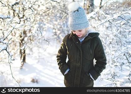 Young girl in snowy landscape, hands in pockets, looking down
