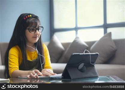 Young girl in spectacles doing her work while attending online class in front of a tablet