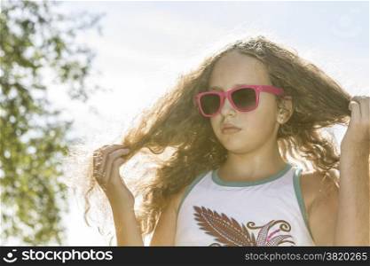 Young girl in sunglasses fixing her long blond hair in the sunlight on a hot afternoon.