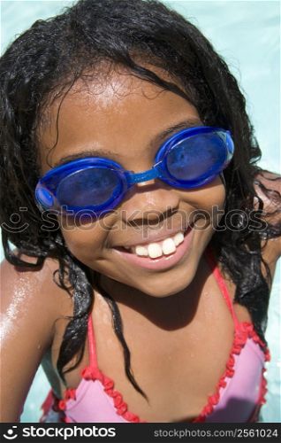 Young girl in swimming pool wearing goggles smiling