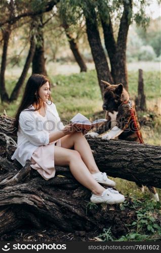 young girl in white clothes sits on a tree in the forest and reads a book