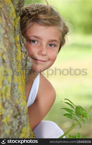 Young girl in white dress hiding behind a tree