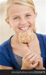 Young girl indoors eating candy apple smiling