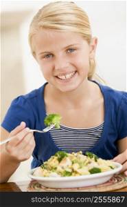 Young girl indoors eating pasta with brocolli smiling