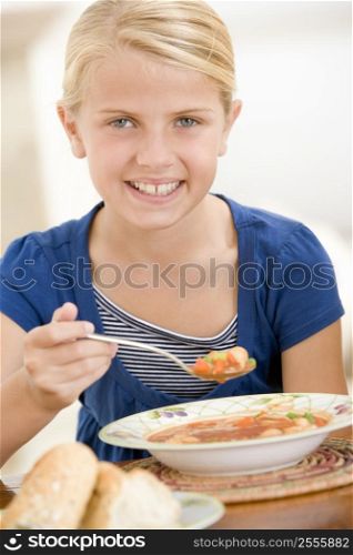 Young girl indoors eating soup smiling