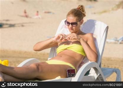 Young girl is lying on a deckchair on a sunny beach and makes nail polish