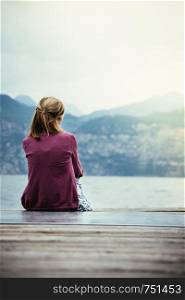 Young girl is sitting on a footbridge and enjoys the view over the lake and the mountains
