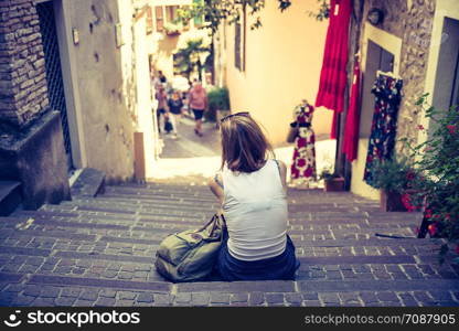 Young girl is sitting on the stony stairs, Italian village, summer holidays