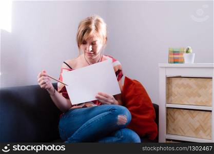 Young girl is sitting with a white text space paper on the sofa