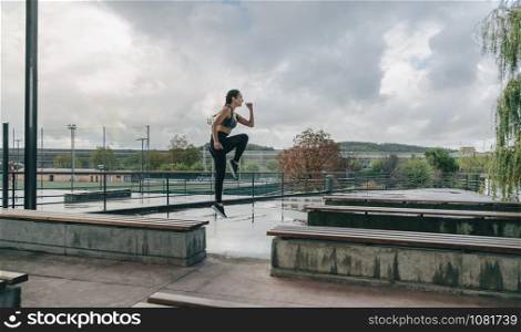 Young girl jumping on benches doing outdoor training on rainy day. Girl jumping on benches doing training