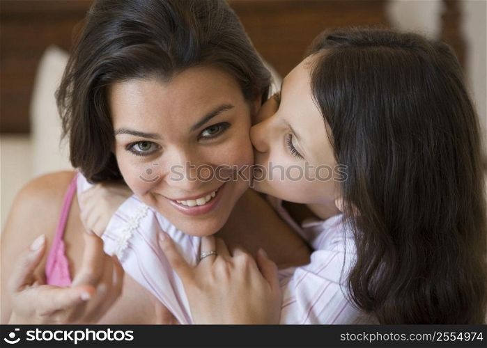 Young girl kissing smiling woman on cheek in bedroom (selective focus)