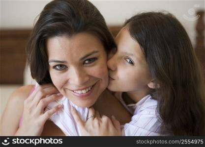 Young girl kissing smiling woman on cheek in bedroom (selective focus)