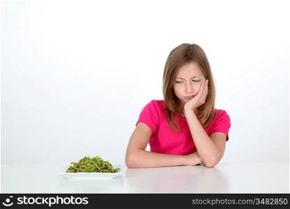 Young girl looking at plate of green beans with disgust