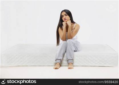 Young girl looking away with hands on chin while sitting on mattress