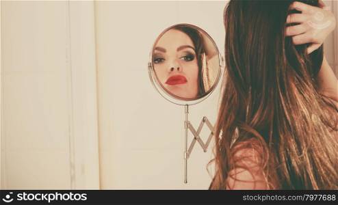 Young girl looking into a mirror.. Young girl looking into a mirror at herself in bathroom. Woman take care about look.