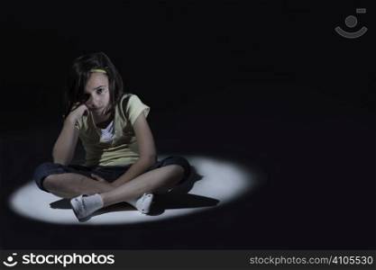 Young girl looking sad sitting in spot light with dark background