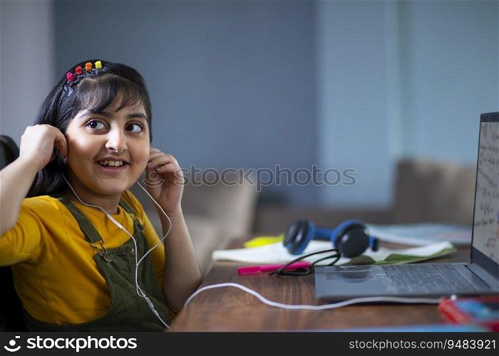 Young girl looking sideways while wearing earphones to attend online class