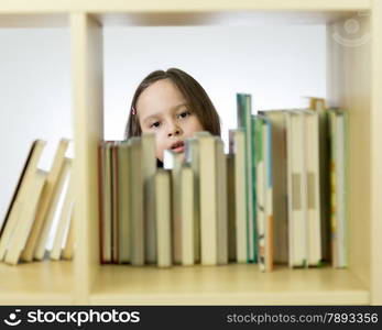 Young girl looking through books in library behind shelf. Horizontal