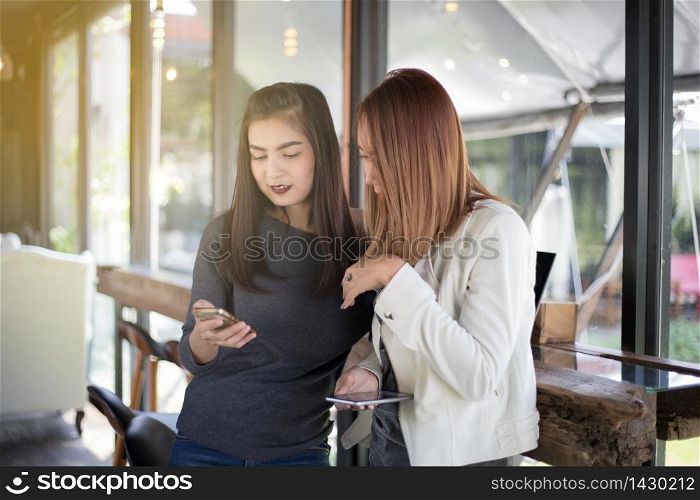 Young girl looking to her friend&rsquo;s phone and feeling exciting and smiling while sitting in living room at office