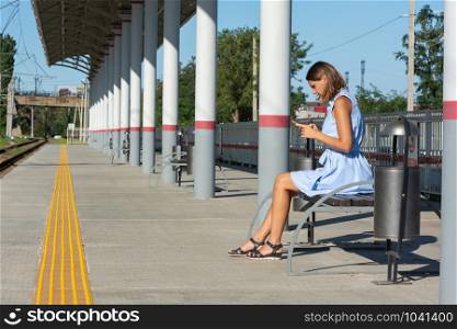 Young girl looks at the phone on the empty platform of the railway station