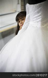 Young girl looks peeks out from behind white gown
