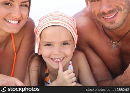 Young girl lying between her parents on the beach