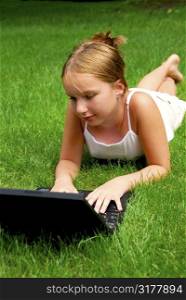 Young girl lying on grass in a park with laptop computer