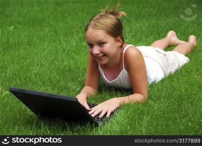 Young girl lying on grass in a park with laptop computer