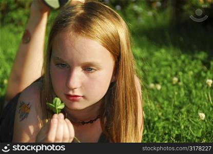 Young girl lying on green grass outside holding a green plant