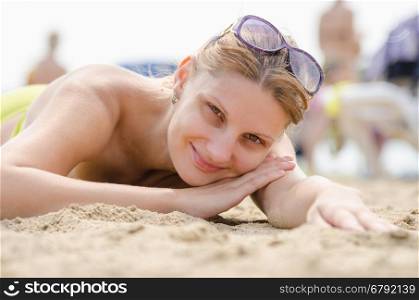 Young girl lying on sandy beach and smiling looks into the frame