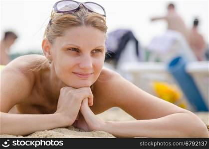Young girl lying on the sandy beach against the backdrop of other travelers and smiling looks into the distance