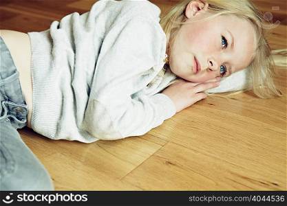 Young girl lying on wooden floor, looking away