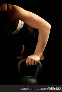 young girl of athletic appearance with black hair is pushing up from an iron kettlebell from a lying position, low key