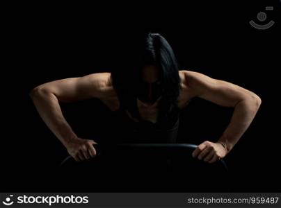 young girl of athletic appearance with black hair is pushing up from the surface on a dark background, athlete's muscular body is tense