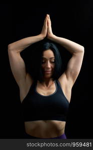 young girl of athletic appearance with black hair raised her hands up and joined her palms, vrikshasana pose, low key