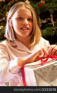 Young Girl Opening Christmas Present In Front Of Tree