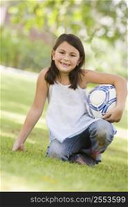 Young girl outdoors at park holding ball and smiling (selective focus)
